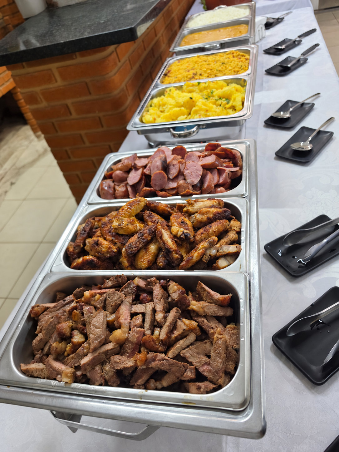 Mesa de buffet com carnes, acompanhamentos e utensílios